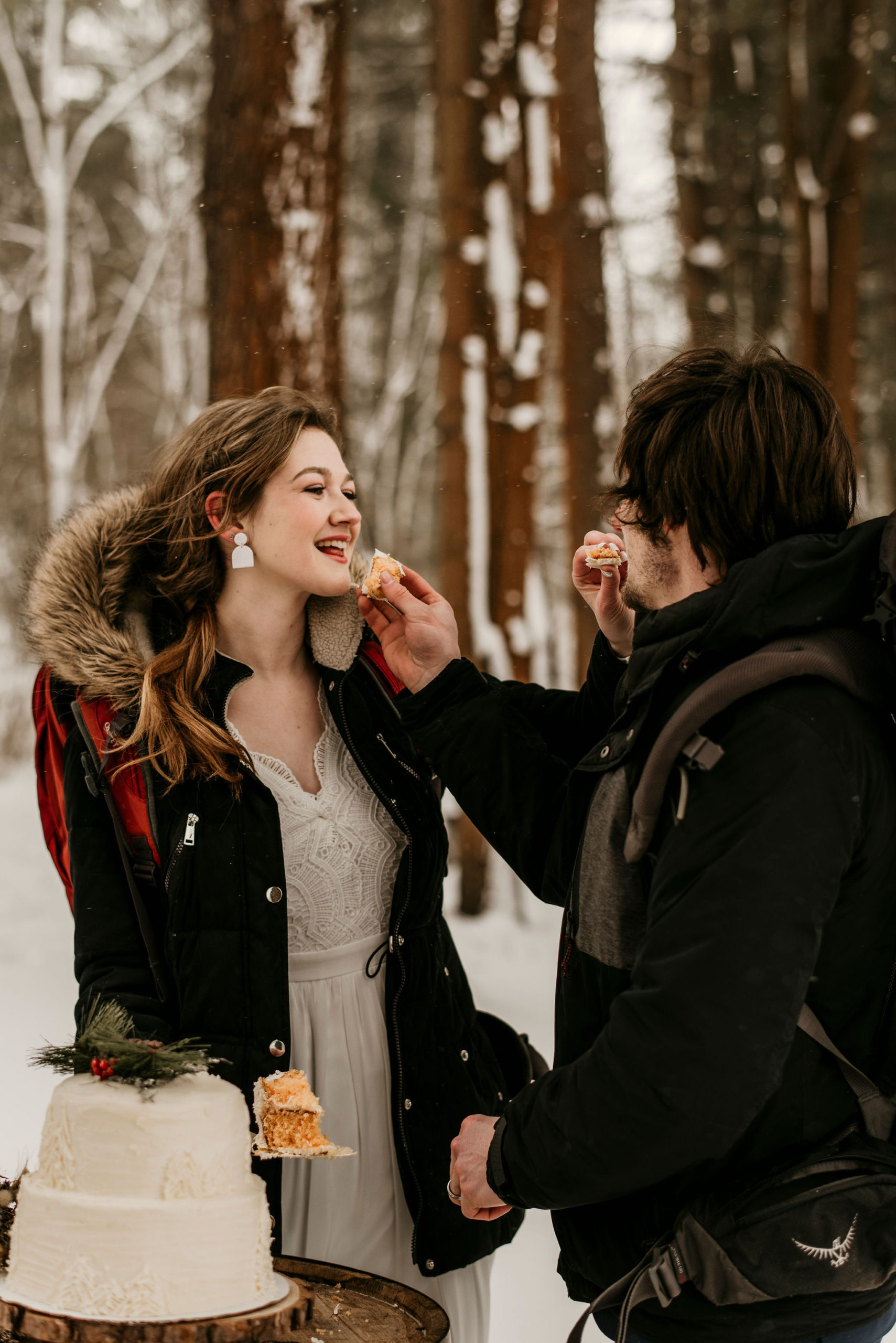 bride and groom feeding eachother cake in a snowy forest
