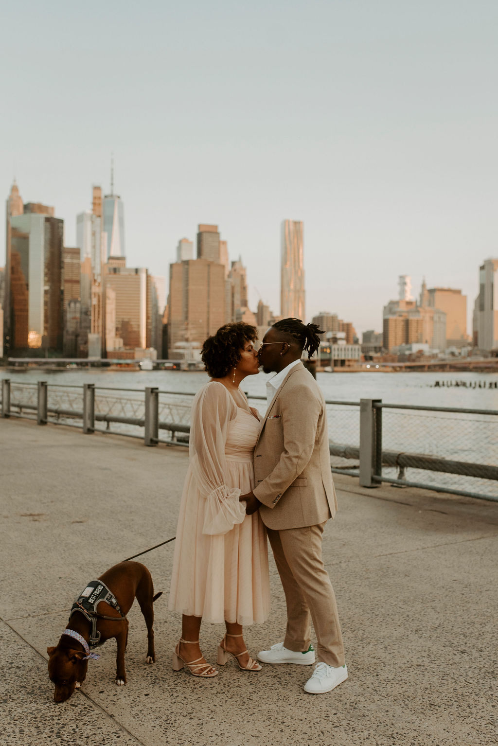 couple kissing while walking their dog with city skyline