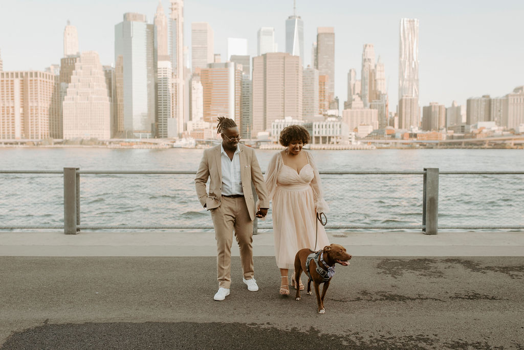 couple standing near the river in new york holding hands and walking their dog