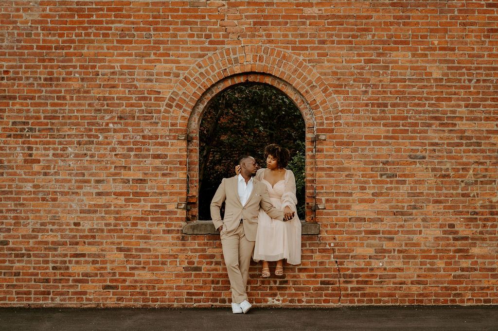 couple sitting near a brick wall and posing in Brooklyn
