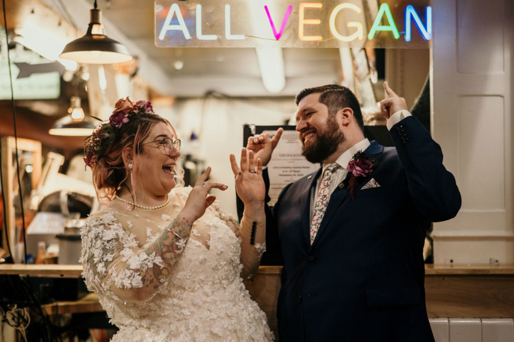 Bride and groom in front of neon ALL VEGAN sign after wedding in PA at The Mütter Museum
