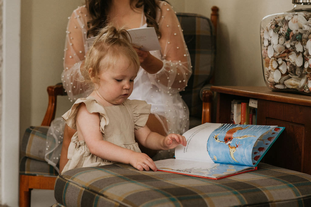 Bride writing vows and daughter reading a book.